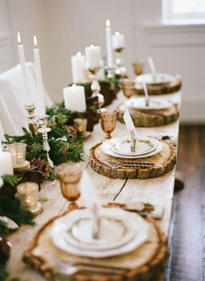 circular wooden place mats, with natural bark, placed on a rustic wooden table, decorated with green foliage, and lit white candles, in different sizes