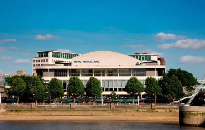 off-white building of the royal festival hall, in london england, made of concrete, and surrounded by multiple green trees