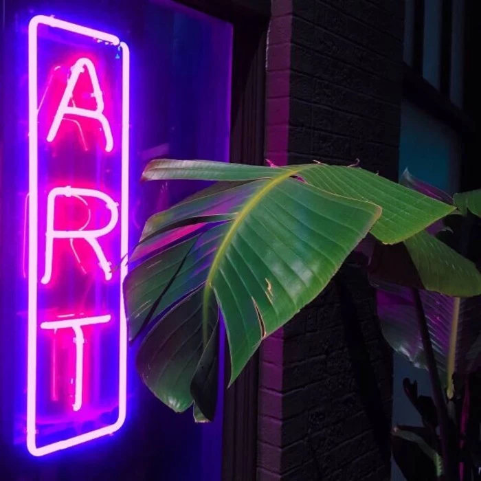 neon sign with the word art, glowing in light pink, 90s grunge aesthetic, near a large green palm leave