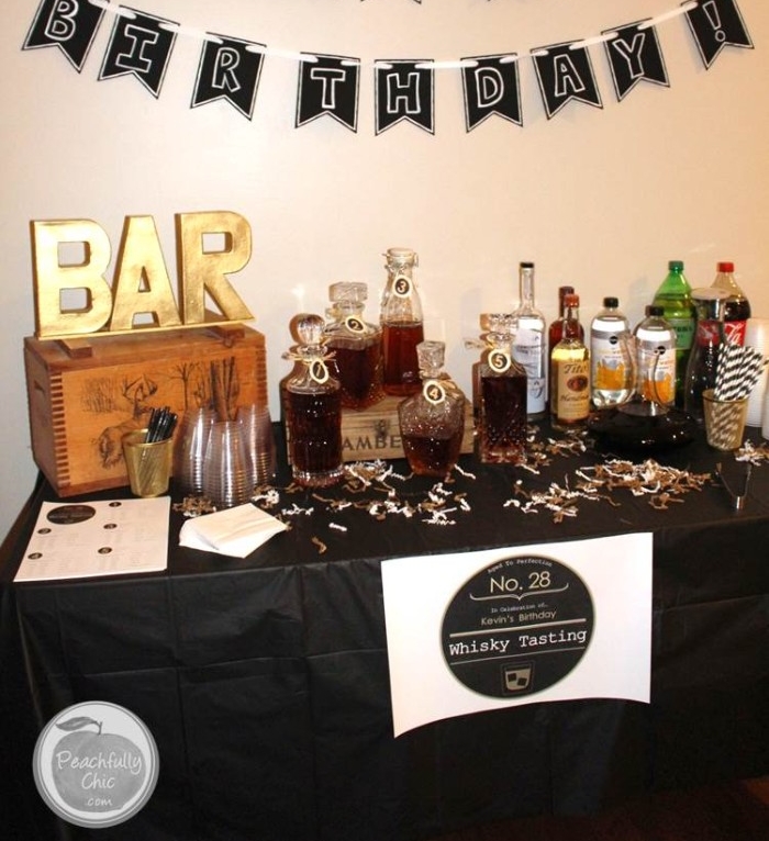 bar written in large gold letters, on top of a wooden crate, placed on a rectangular table, with a black tablecloth, and a variety of different bottles, 50th birthday celebration ideas for husband, whiskey tasting experience