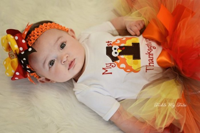 turkey cartoon in yellow, orange and dark brown, printed on a white onesie, worn with a fluffy tulle tutu skirt, in yellow and orange and brown, baby girl thanksgiving outfit, orange headband with three multicolored bows