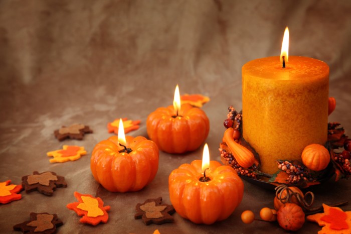 small lit candles, shaped like pumpkins, near a larger, cylinder shaped orange candle, thanksgiving card messages, small decorative autumn leaves, made from felt