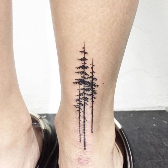 simple design featuring three tall, and narrow pine trees, tattooed in black, on the back of a person's ankle