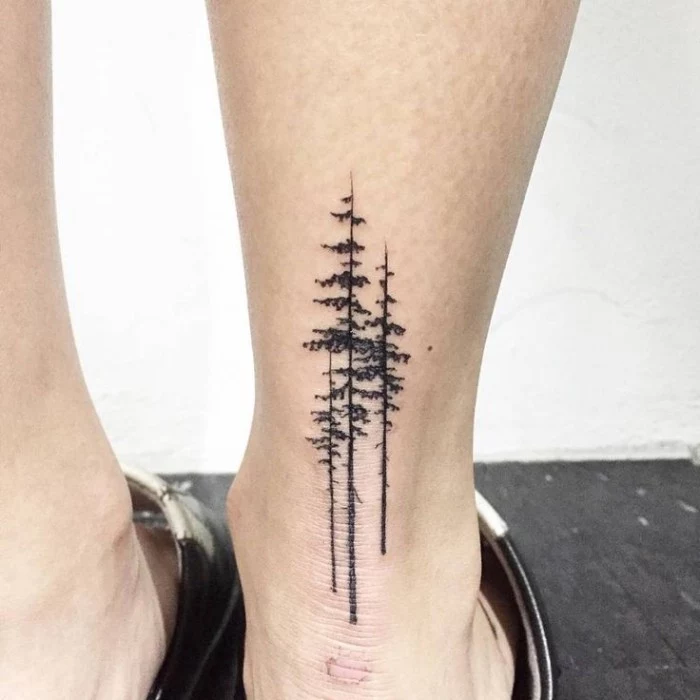 simple design featuring three tall, and narrow pine trees, tattooed in black, on the back of a person's ankle