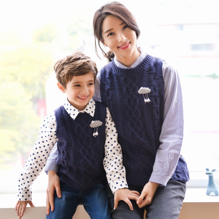 son and mother, sitting side by side, dressed in similar outfits, patterned shirts in white and dark blue, identical navy cable knit vests, with matching pins, and blue jeans