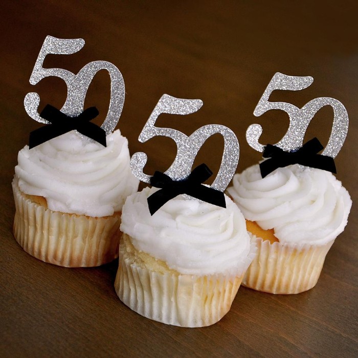silver glitter toppers, shaped like the number 50, and featuring small black bows, decorating three vanilla birthday cupcakes, with creamy white frosting