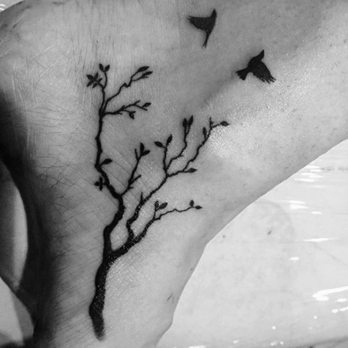 pair of flying birds, above a three with several branches, black ink tattoo, on a person's foot and ankle, small tattoos with meaning