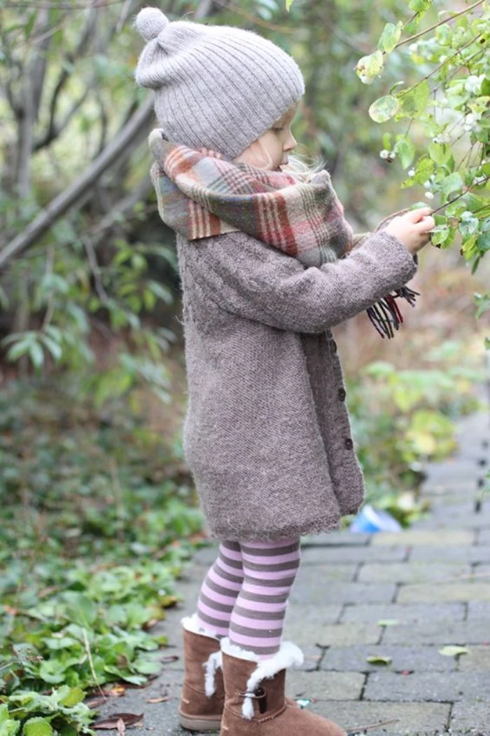 toddler thanksgiving outfit, grey cardigan and a plaid blanket scarf, striped leggings in pale pink and dark purple, beige shearling fur boots, and a light grey beanie hat