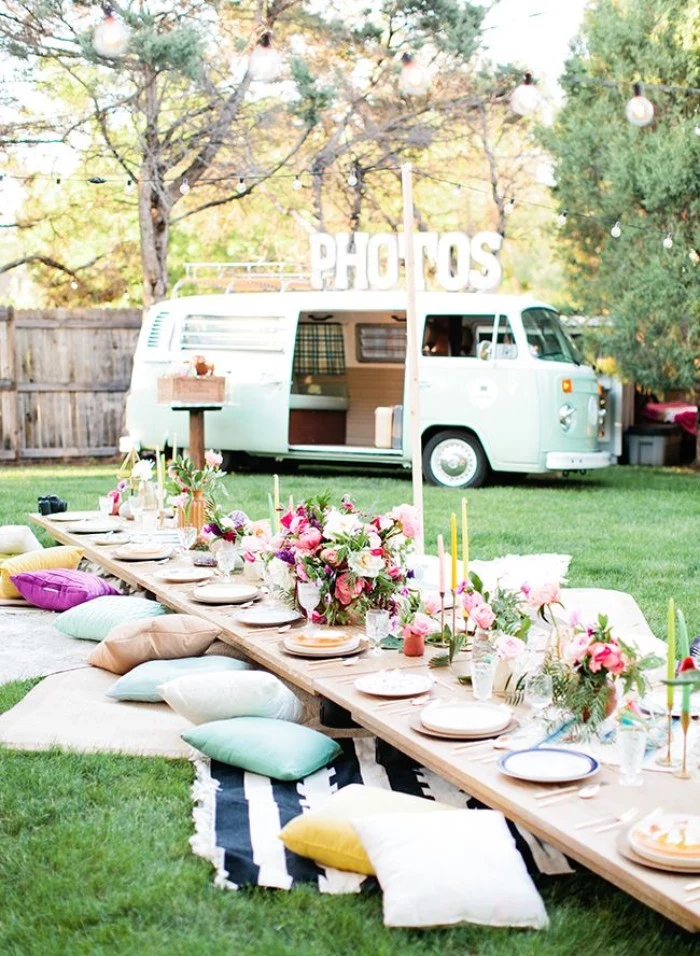 boho style garden party, with a low wooden table, set for a festive meal, with plates and flowers, and surrounded by blankets and cushions, 50th birthday ideas, light blue van nearby