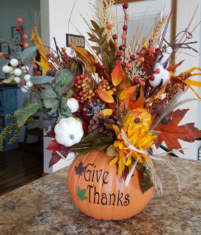plastic orange pumpkin, with the inscription give thanks, filled with faux fall leaves, pinecones and berries, cotton and wheat stalks, and many others