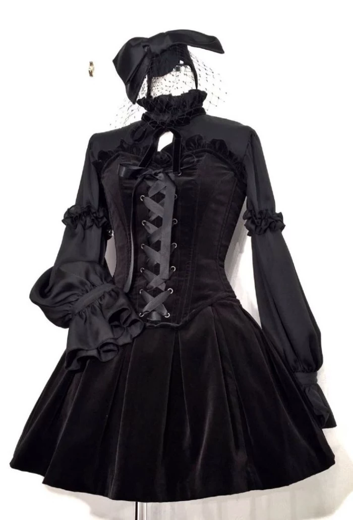 velour lolita style dress in black, with frilly sleeves, and a lace up corset detail, small face veil made from black mesh, and a large black hair bow