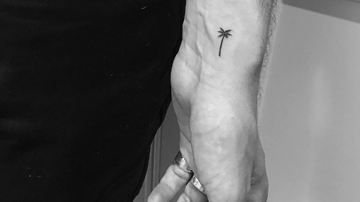 tiny palm tree, tattooed in black, near the wrist of a man's hand, forearm tattoos, seen on a black and white photo