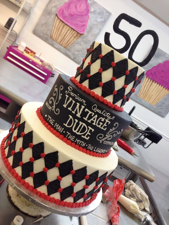 multi-layered cake in black and white, with red details, and a topper shaped like the number 50, vintage dude written in white frosting
