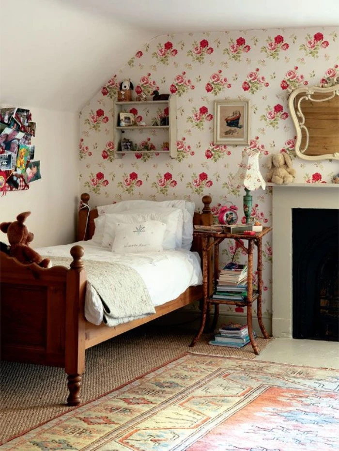 wallpaper with a floral pattern, decorating one wall of a bright room, containing a vintage style wooden bed, cool beds for teens, fireplace and an ornamental rug