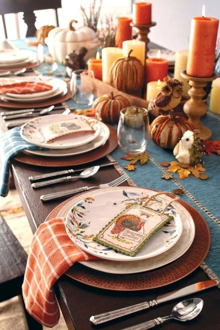 place holder cards, with colorful turkey illustrations, on top of stacked plates, on a table decorated with lit, yellow and orange candles