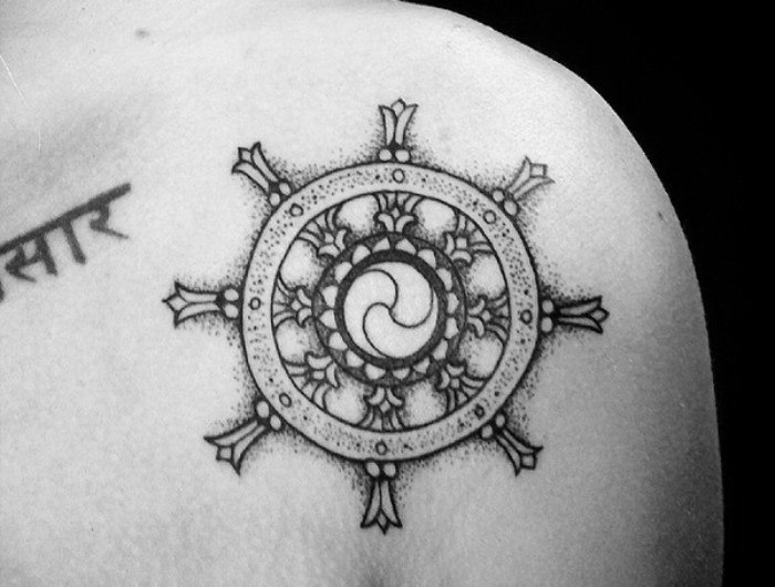 dharmachakra tattoo in black, the wheel of dharma, a sacred symbol in hinduist faith, small tattoos with meaning, on a person's shoulder