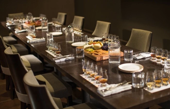 long wooden table, set for ten people, with five small glasses in front of each chair, 50th birthday party ideas, whiskey tasting with fruit and cheese