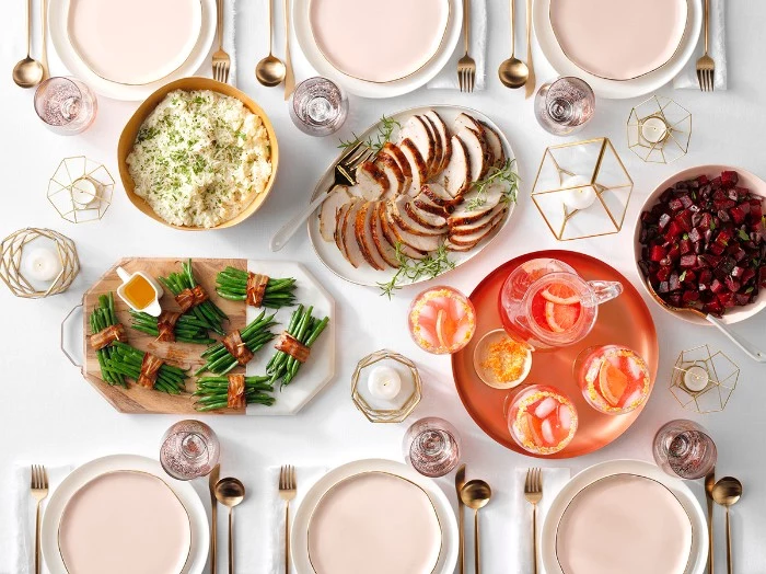 rose gold cutlery, on a table with pale pink and white plates, white tablecloth and several dishes, thanksgiving wishes, roast turkey slices, asparagus with bacon, and others