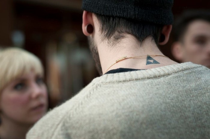 man dressed in a pale grey sweater, with his back to the camera, a black triangle tattoo, with a smaller, white reversed triangle inside, small tattoos for men, on the back of his neck