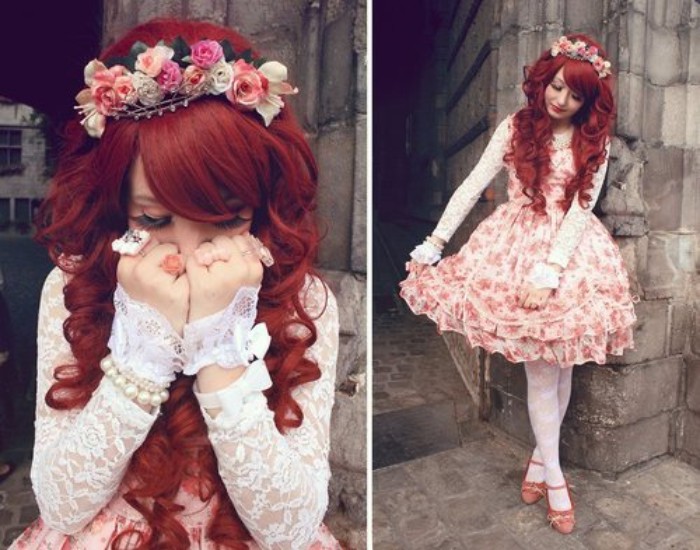 red wig with curls and side bangs, worn by a young woman, in a floral pink sweet lolita dress, with white lace sleeves