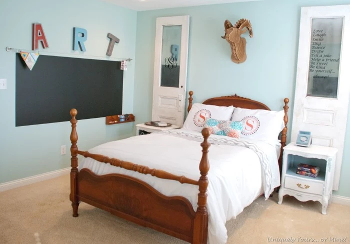 antique style bed, made of wood, and featuring white bedding, and pillows in pale pink, light blue and white, cool beds for teens, in a room with pale blue walls, decorated with a blackboard, and other items