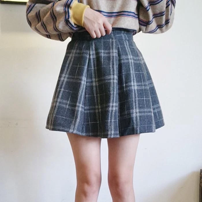 grunge definition, slim young woman, dressed in a woolen, grey plaid mini skirt, and a beige oversized jumper, with blue stripes, and yellow cuffs
