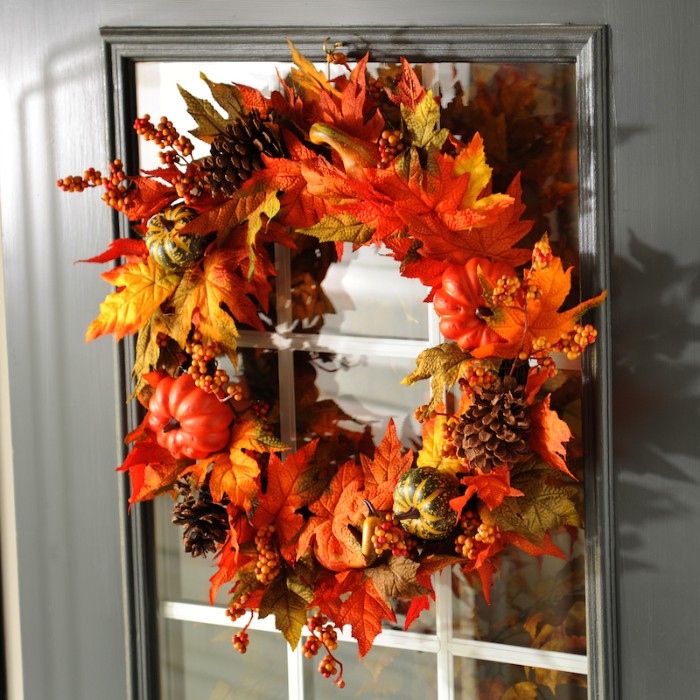 fall wreath made from faux leaves in yellow, orange and pale green, thanksgiving greeting message, decorated with pine cones, small fake pumpkins, and tiny orange berries