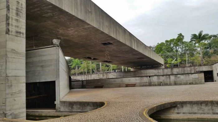grounds of the brazilian museum of sculpture in sao paulo, yard covered in stone pavement, with a large concrete bridge overhead