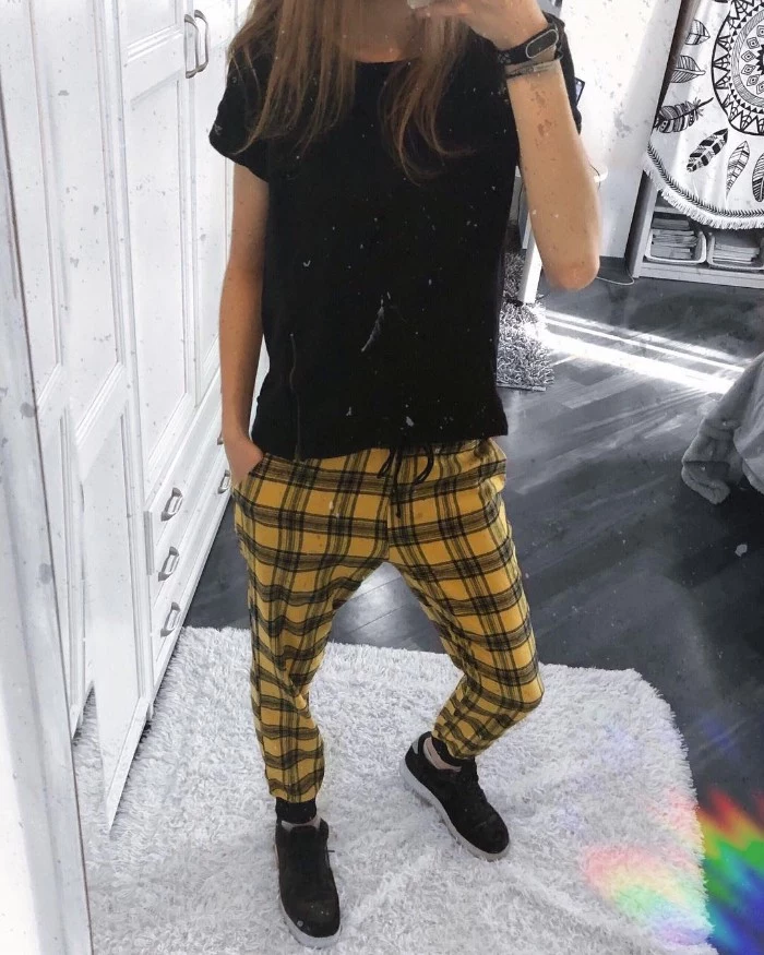 slim woman dressed in a black t-shirt, yellow checkered trousers, and black sneakers, grunge definition, taking a mirror selfie