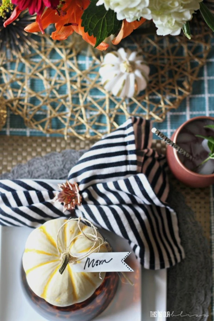 tiny yellow pumpkin, with a white label, featuring the inscription mom, tied to its stem, striped black and white napkin