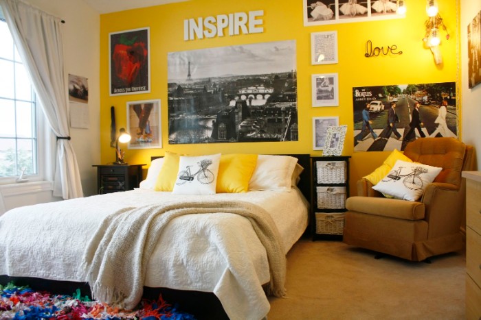 armchair in beige, and a large bed in white, near a yellow wall, decorated with posters, framed images and words