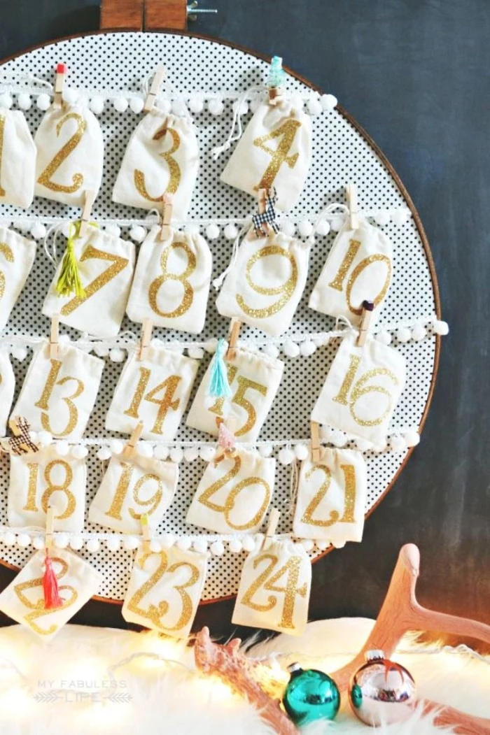 embroidery hoop with white and black fabric, decorated with 24 drawstring pouches, attached to pieces of white lace ribbon, christmas advent calendar diy idea