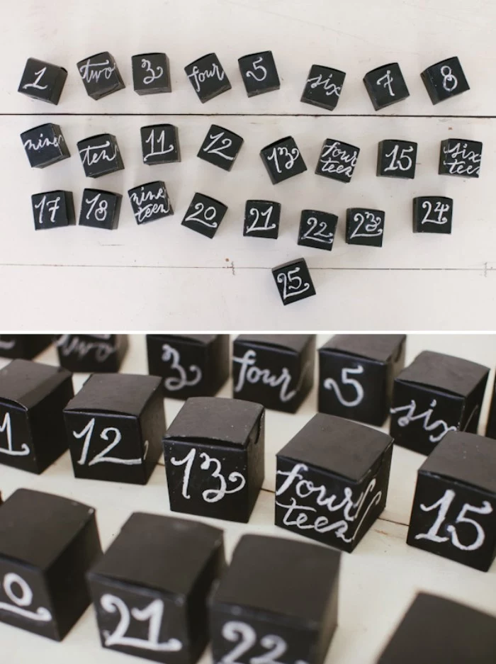twenty five black, cube-shaped boxes, each decorated with a different number, written by hand, with white chalk, diy advent calendar, next image shows a close up of the boxes