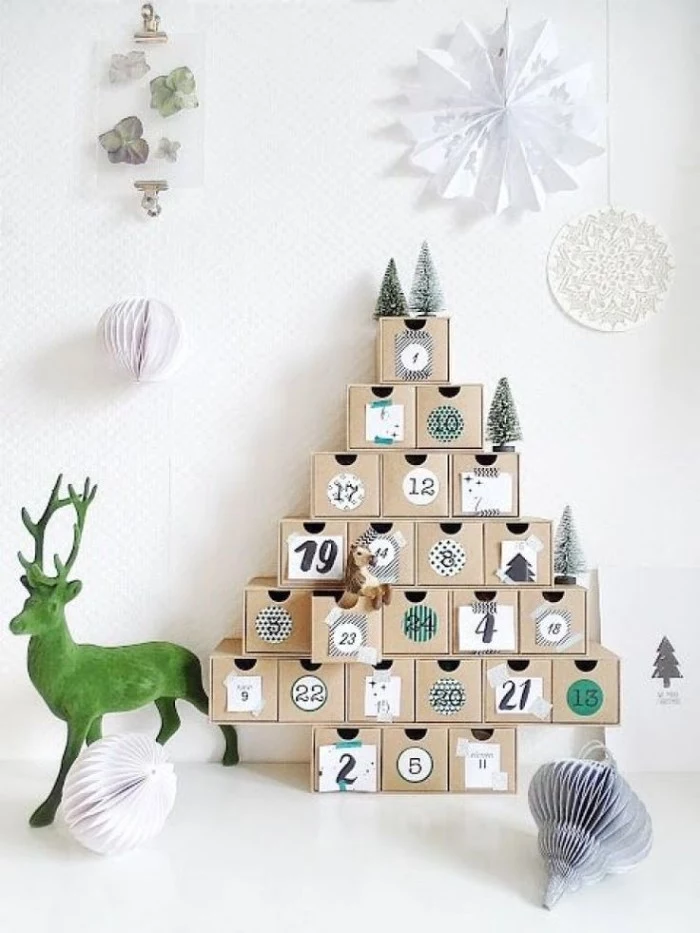 reindeer figurine in green, next to an advent calendar, made from multiple, numbered pale beige, cube-shaped boxes, stacked in a christmas tree shape