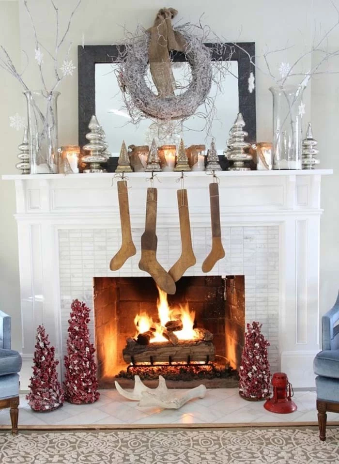 rustic antique looking beige stockings, hanging on a white mantelpiece, decorated with silver ornaments, and lit candles,