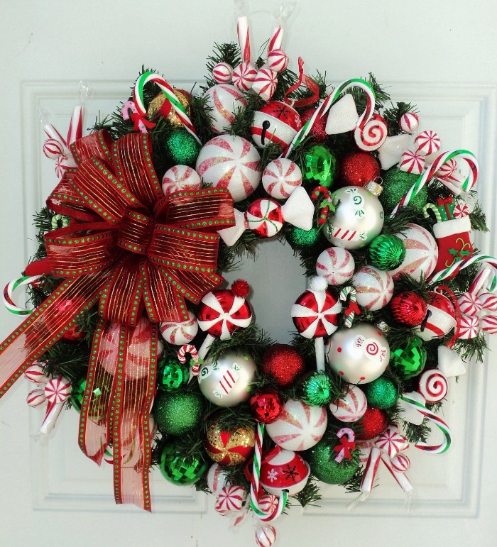 big bow made from sheer red ribbon, with green details, ona diy christmas wreath, decorated with candy canes, and baubles in green and red, white and gold