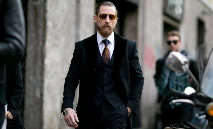 black tie optional, bearded man with dark yellow sunglasses, wearing a black three piece suit, with a white shirt, and a black and yellow tie