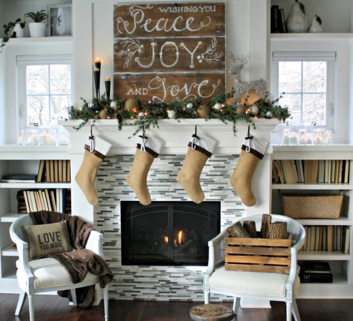 wishing you peace, joy and love, written in white, on a wooden board, placed above a fireplace, images of christmas, four beige stockings and lit candles