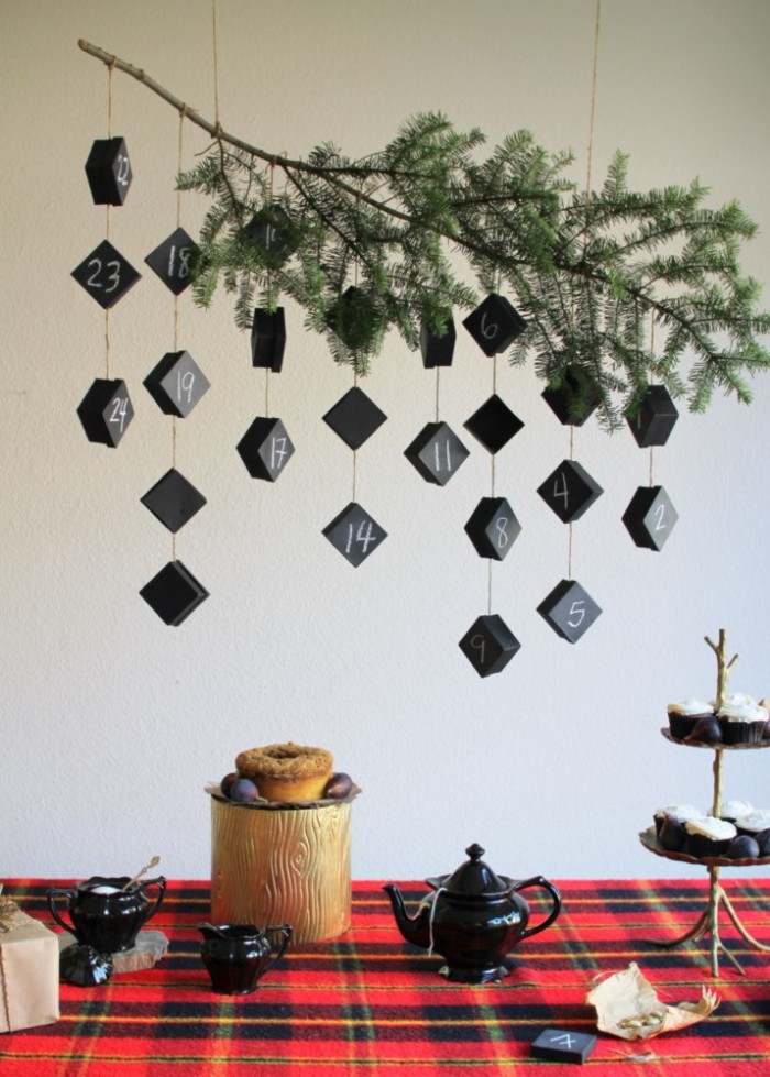 branch of a fir tree, decorated with several pieces of string, each tied to two or more, small black boxes, numbered with white chalk, advent calendar ideas, hanging over a table 