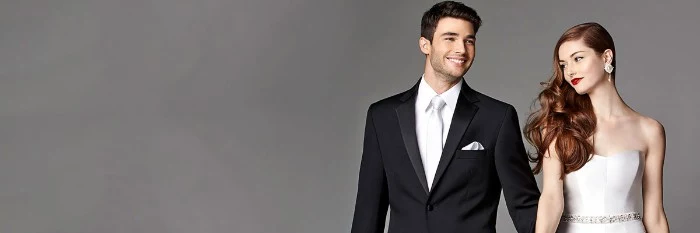 silver tie worn with a white shirt, and a black dinner jacket, with a silver handkerchief, black tie optional, worn by a smiling groom, standing hand in hand with a bride, dressed in a light silver strapless dress