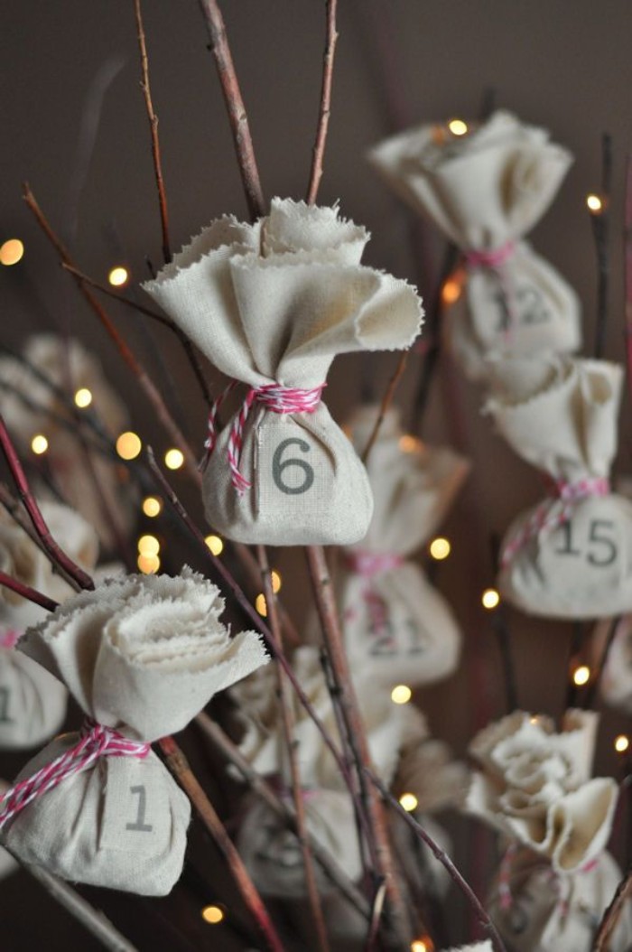 little numbered bundles, made from light cream fabric, tied with a striped, red and white string, attached to dry brown branches, decorated with small, glowing fairy lights