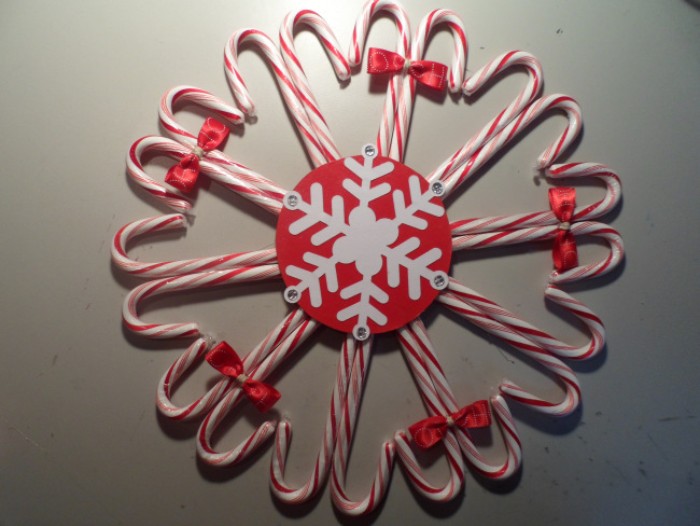 how to make a christmas wreath, candy canes in white, with red swirly stripes, stuck together to form a wreath, decorated with a red circle, and a white snowflake, in the middle