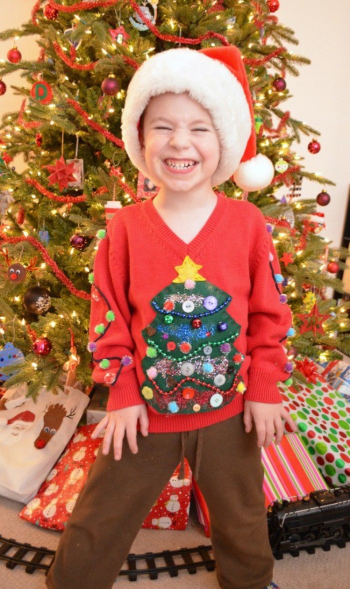boy wearing a red v-neck jumper, decorated with a christmas tree motif, made from green and yellow felt, and decorated with beads in different colors, diy ugly christmas sweater for kids