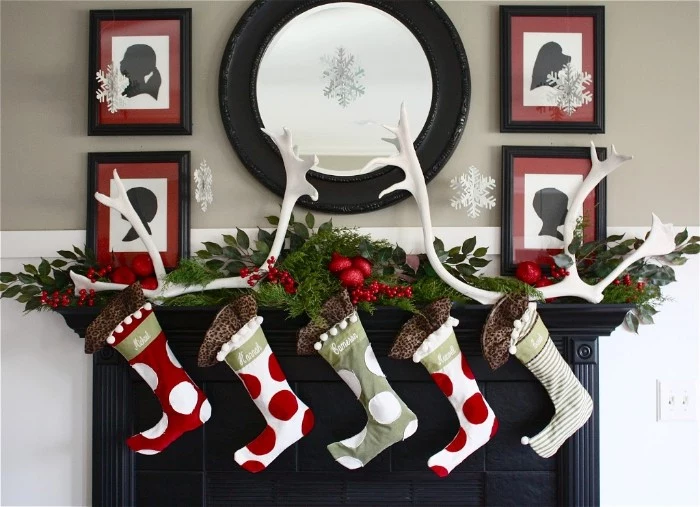 white antlers and five stockings, in red and white and grey, decorated with red and white polka dots, and white and grey stripes, on a christmas fireplace, four framed artworks and a round mirror