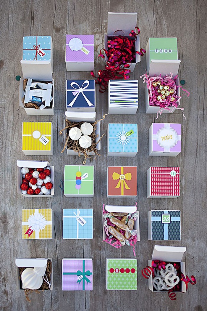 square boxes in different colors, placed on a grayish wooden surface, some of the boxes are opened, revealing treats and christmas ornaments