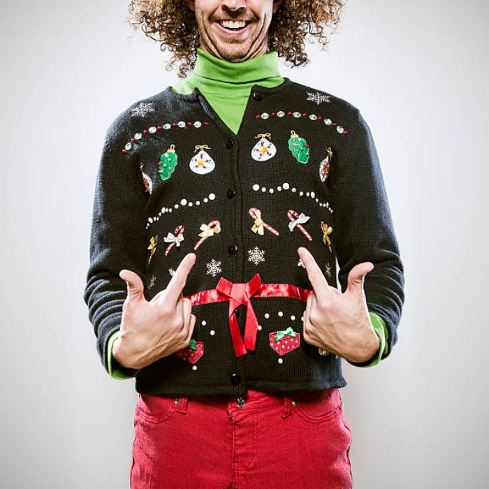 ugliest christmas sweater, man with medium length, brown curly hair, wearing a light green turtleneck, coral red trousers, and a black cardigan, with colorful festive motifs, and a shiny red ribbon
