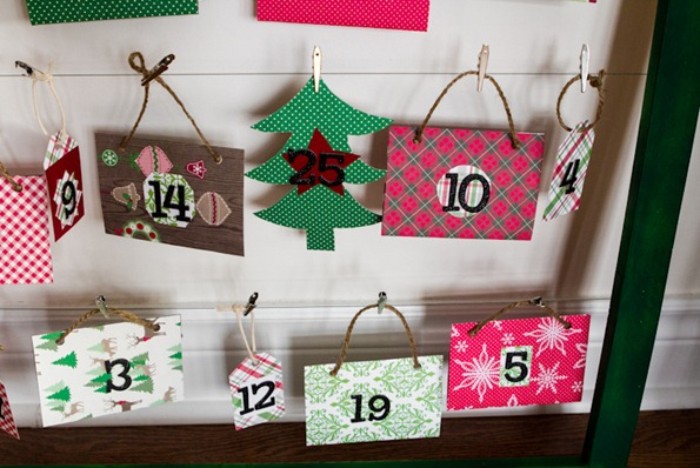 countdown to christmas calendar, made with numbered, colorful patterned pieces of card, some featuring cord handles, attached with miniature pegs, to of wire or string