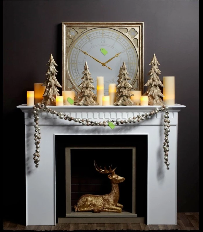 ten faux glowing candles, on a white mantelpiece, next to four christmas tree statuettes, a large antique clock, and a silver garland, reindeer statuette in gold