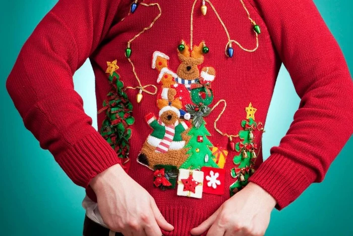 close up of a red jumper, decorated with multiple festive applique details, in various colors, ugliest christmas sweater, reindeer and xmas trees, presents and string lights