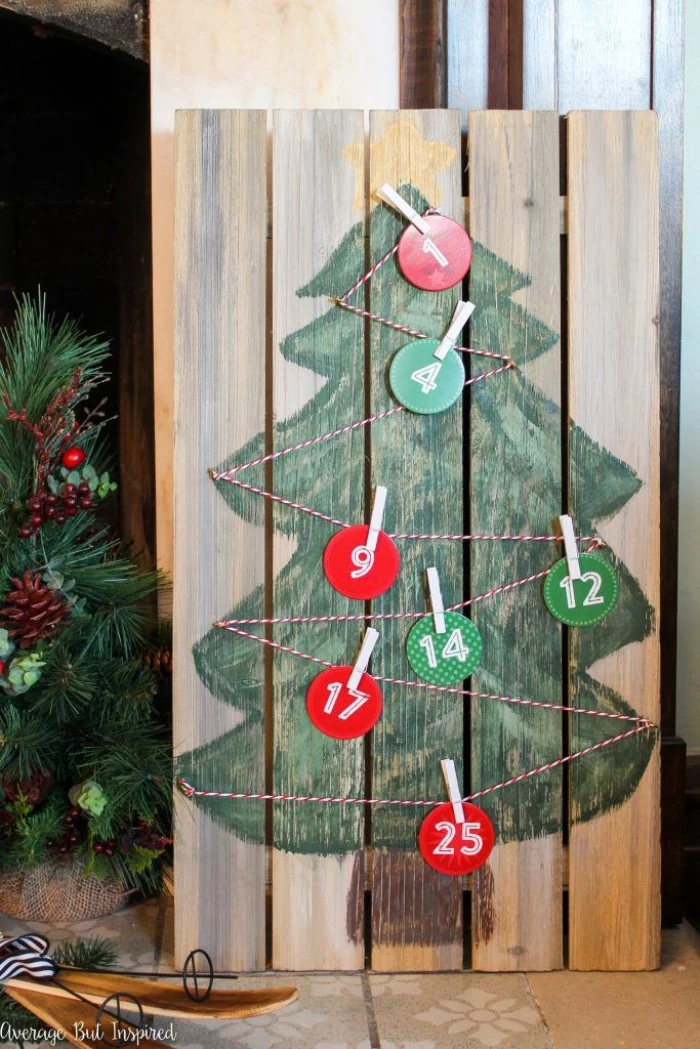 pallet made of wood, with a simple, child-like drawing of a christmas tree, decorated with striped, red and white string, featuring round numbered labels, in different colors, attached to the string with clothes pegs, fun advent calendars diy